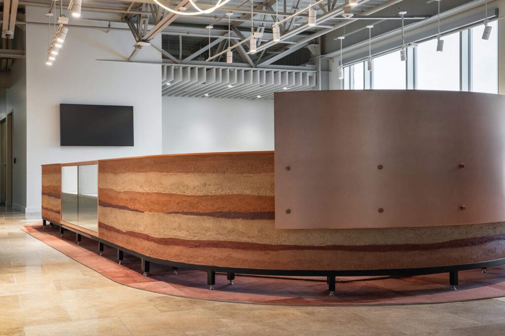 A sweeping curved reception desk featuring an intricate rammed earth clay plaster finish inside an Austin lobby space.