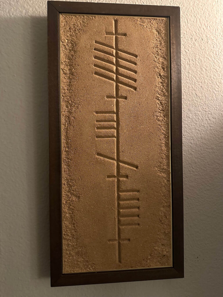 A detailed close-up shot showing the granular texture and carved lines of ancient Irish Ogham script on an earthen clay plaster art piece.