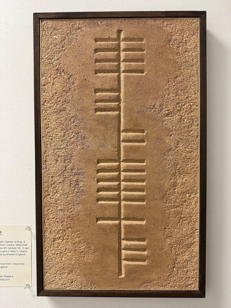 A custom framed clay art piece featuring the ancient Celtic Ogham writing that translates into "Fáilte", the traditional Irish Gaelic word for "welcome", carved into highly textured earthen plaster.